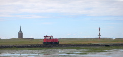 De locomotief van Wangerooges smalspoorbaan. Op de achtergrond de oude en de nieuwe Westturm.